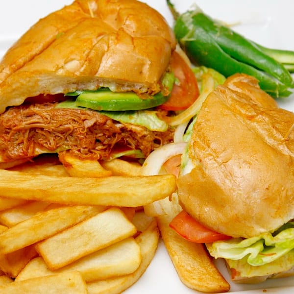 Two Mexican tortas with shredded meat, avocado, lettuce, tomato, and onions, served with fries and jalapeños.