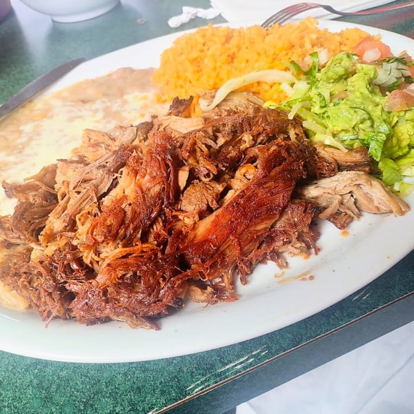 A plate of Sergio's Mexican Restaurant's carnitas with rice, refried beans, guacamole, and salad.