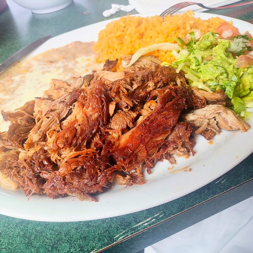 A plate of Sergio's Mexican Restaurant's carnitas with rice, refried beans, guacamole, and salad.