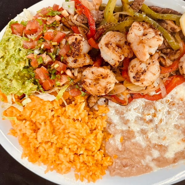 A plate of Sergio's Mexican Restaurant fajitas with shrimp, steak, bell peppers, rice, beans, guacamole, and pico de gallo.
