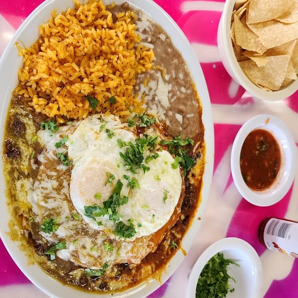 Huevos Rancheros with rice, beans, salsa, and tortilla chips on a vibrant pink table.